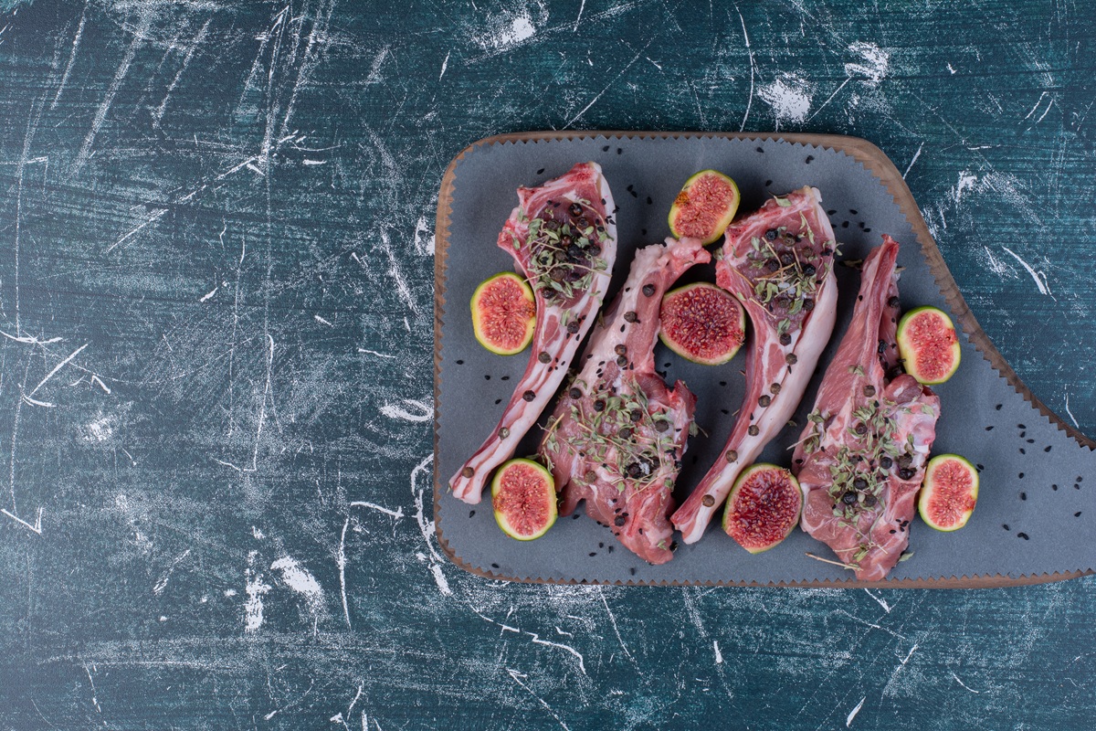 raw ribs in wooden board with figs and dried herbs